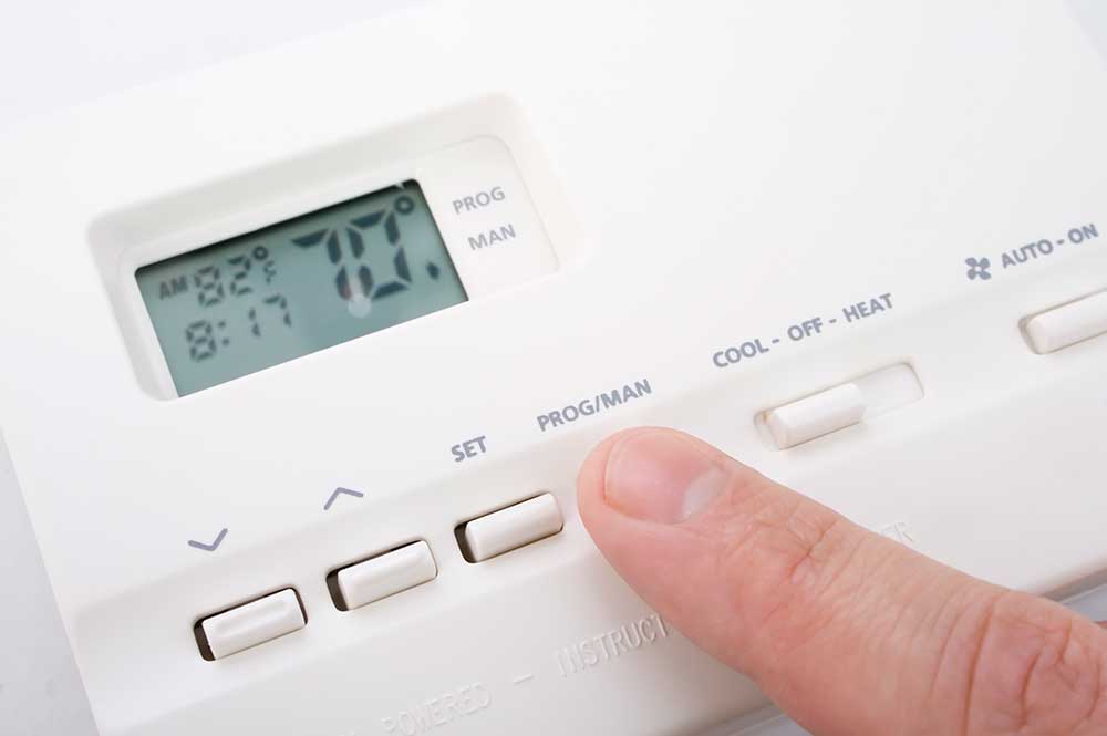 finger pressing button to change temperature on thermostat 